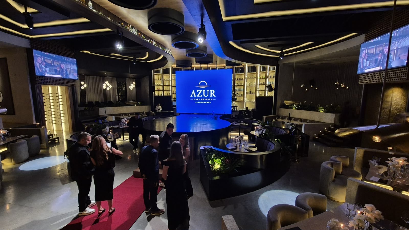 Salón con tarima circular, pantalla LED central y alfombra roja de ingreso